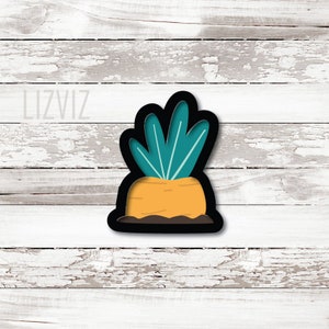 May include: A black cookie cutter shaped like a carrot with green leaves. The carrot is orange and the leaves are teal.