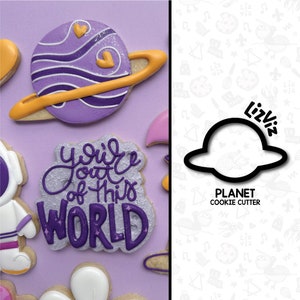 May include: Purple and yellow cookie decorated with a planet design. The cookie is next to a cookie that says "you're out of this world". A cookie cutter in the shape of a planet is shown on the right side of the image.