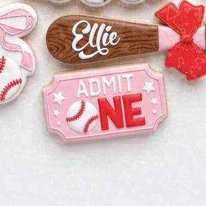 May include: A set of decorated sugar cookies featuring a brown baseball bat with the name Ellie in white script and a large red bow, alongside a pink rectangular ticket cookie with the text ADMIT ONE and a white baseball graphic with red laces.