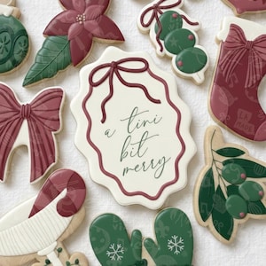 Puede incluir: Surtido de galletas de Navidad decoradas. Las galletas incluyen un lazo, una flor de pascua, un calcetín, una ramita de aceitunas y un guante. Una galleta tiene el texto "a tini bit merry" en escritura verde dentro de un borde burdeos.