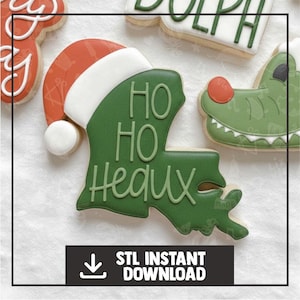 Könnte beinhalten: Eine Sammlung dekorierter Zuckerkekse. Ein Keks hat die Form des Bundesstaates Louisiana, mit einem Weihnachtsmannhut und den Worten "Ho Ho Heaux" in grüner Glasur. Weitere Kekse sind ein Alligator und ein Keks mit dem Wort "Dolph" in grüner Glasur.