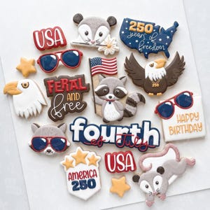May include: A collection of decorated sugar cookies in various shapes and designs. The cookies include patriotic themes such as the USA, an American flag, an eagle, and the text "Fourth of July". Other cookies feature animals and sunglasses.