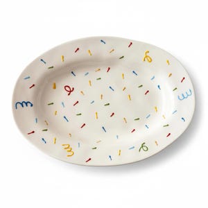 May include: An oval-shaped white ceramic serving platter featuring a scattered pattern of small, colourful painted dashes and several hand-painted squiggly lines in shades of red, blue, yellow, and green across the entire surface of the dish.