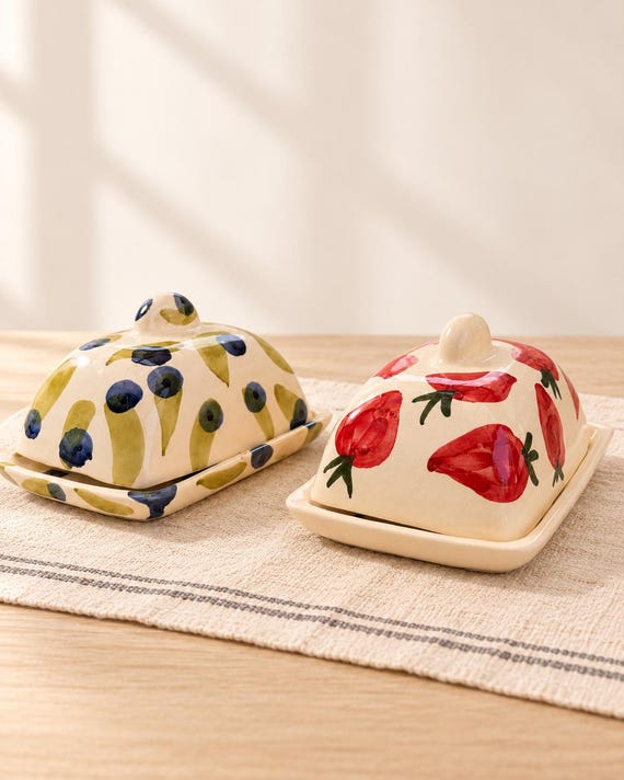 Hand-painted artisan ceramic butter dish where the lid IS the art — strawberry or olive motifs make it a countertop centerpiece, not just a butter keeper.