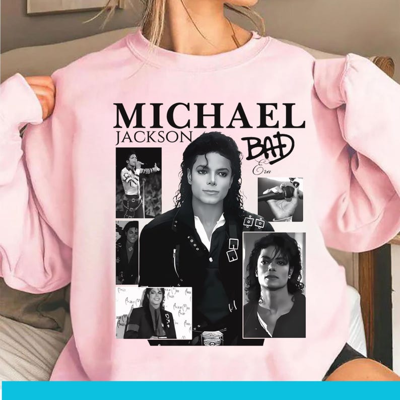 May include: Pale pink sweatshirt with a collage of images of Michael Jackson. The design includes the text "MICHAEL JACKSON BAD" in black. The collage includes black and white photos of the singer.