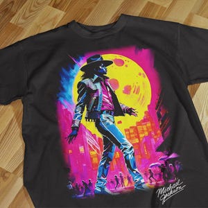 Pode incluir: T-shirt preto com uma ilustra&ccedil;&atilde;o vibrante de uma figura com chap&eacute;u e casaco, num cen&aacute;rio urbano com uma grande lua amarela. O gr&aacute;fico &eacute; em tons de azul, rosa e amarelo, com o nome "Michael Jackson" numa assinatura.