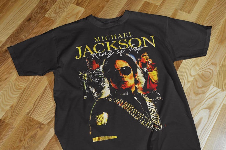 Pode incluir: Camiseta preta com um gr&aacute;fico dourado de Michael Jackson usando &oacute;culos de sol e o texto "MICHAEL JACKSON King of Pop". O design inclui imagens de Jackson em v&aacute;rias poses.