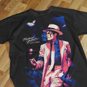 Pode incluir: Camiseta preta com um gr&aacute;fico de Michael Jackson de terno e chap&eacute;u brancos, com o texto "Michael Jackson Smooth Criminal". A imagem tem um estilo retro pop art.