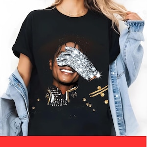 May include: Black t-shirt with a portrait of a smiling person, one eye covered by a sparkling, bejeweled glove. The person is wearing a black jacket with gold detailing. The image is a close-up, focusing on the face and upper body.
