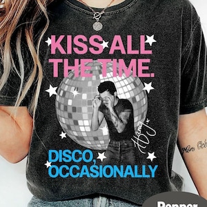 Peut inclure: T-shirt gris foncé avec l'inscription rose "KISS ALL THE TIME" et un motif boule à facettes. En dessous, le texte bleu "DISCO, OCCASIONALLY". Des étoiles blanches entourent les graphiques.