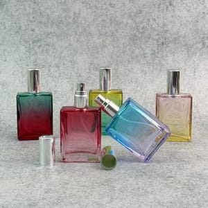 May include: A collection of rectangular glass perfume bottles with silver spray tops. The bottles are in various colors, including red, green, yellow, and blue, with a gradient effect. One bottle has its cap off.