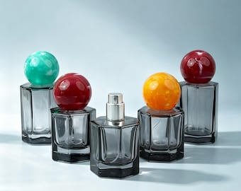 Frasco de perfume em vidro cinza fumê de 30ml e 50ml com atomizador hexagonal em formato de cubo e tampa esférica com efeito espiral colorido. Frasco vazio e recarregável para spray de fragrância.
