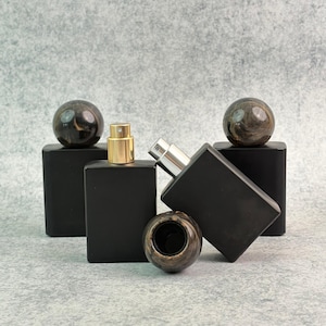 May include: Black rectangular perfume bottles with gold and silver sprayers. Each bottle has a matching dark, patterned sphere on top. One bottle has a matching sphere as a cap.