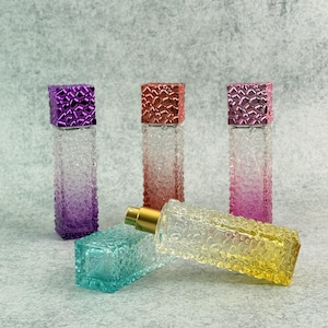 May include: An assortment of colorful perfume bottles. The bottles are rectangular with textured glass and feature a gradient color scheme. The lids are square and metallic. One bottle is yellow, another is turquoise, and the others are purple, pink, and red.