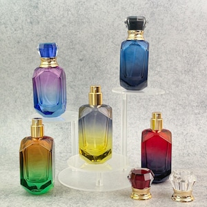 May include: A collection of colorful perfume bottles with gold-colored sprayers and decorative caps. The bottles display a gradient of colors, including blue, purple, yellow, green, and red. The bottles are displayed on clear acrylic stands.