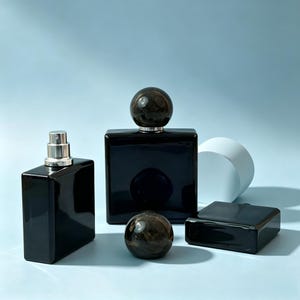 May include: Three black glass perfume bottles with a glossy finish. One bottle is rectangular with a silver spray nozzle, another is square with a round, marbled black and gold cap, and the third is a flat rectangular bottle lying on its side.