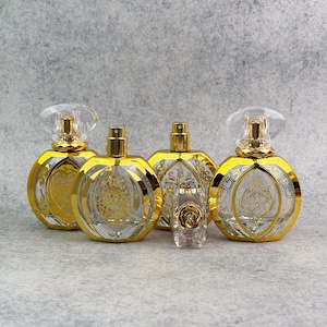 May include: A collection of perfume bottles with gold detailing. The bottles have clear glass bodies with gold accents and spray nozzles. The larger bottles have clear, faceted stoppers. A smaller bottle with a rose design is also present.