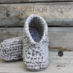 Puede incluir: Un par de pantuflas de estilo cottage de crochet para niños. Las pantuflas están hechas con un hilo texturizado y tienen un diseño sencillo. El patrón está disponible para descargar digitalmente. "Kids Cottage Slipper Crochet Pattern digital download" y "Prairie Yarn Creations" están escritos en la imagen.
