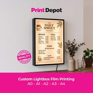 May include: A rectangular black lightbox displaying a cafe menu titled The Daily Sprout with sections for brews, teas, and food. The menu features illustrations of a coffee cup, leaves, and an avocado. A pink circular premium quality seal is visible.
