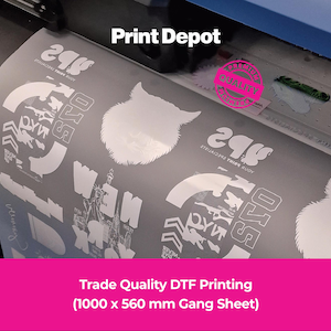 May include: A large format printer producing a 1000 x 560 mm DTF gang sheet featuring white graphic designs, including a wolf head silhouette, New York text, and the Print Depot logo. The sheet is being fed through the machine for professional printing.