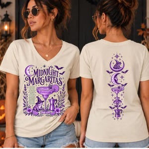 May include: A cream-colored V-neck t-shirt featuring a purple graphic design. The front displays the text Midnight Margaritas, a frog in a witch hat, a margarita glass, and a coffee pot. The back shows a vertical arrangement of these icons.