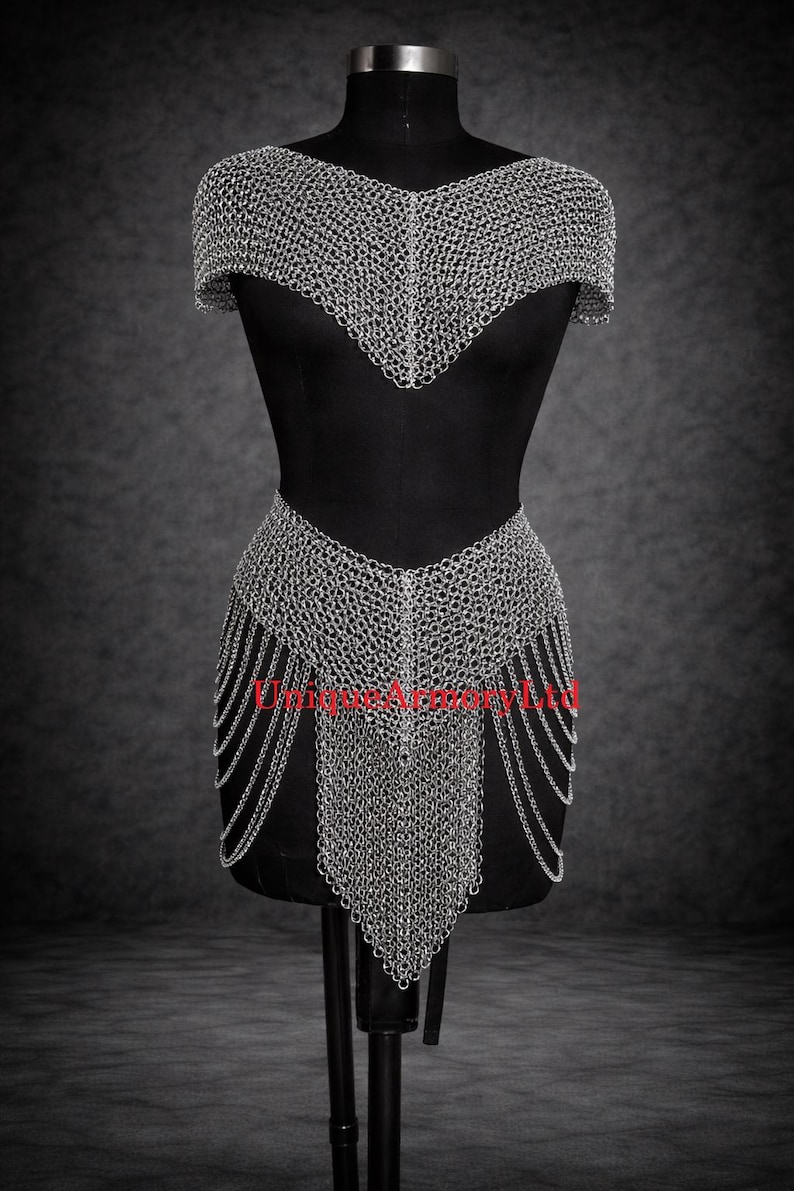 Pu&ograve; includere: Un indumento in cotta di maglia argentata composto da una parte per le spalle a maniche corte e una parte per la vita abbinata con frange di catene pendenti. Le maglie metalliche formano uno scollo a V. Il testo UniqueArmoryLtd &egrave; visibile.