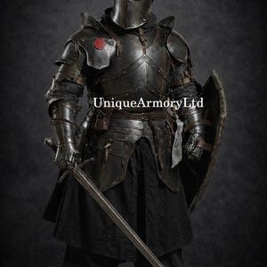 K&ouml;nnte beinhalten: Eine komplette schwarze mittelalterliche R&uuml;stung, einschlie&szlig;lich Helm, Brustplatte und Beinschutz. Der Ritter h&auml;lt ein langes Schwert und einen Schild. Der Text "UniqueArmoryLtd" ist sichtbar.