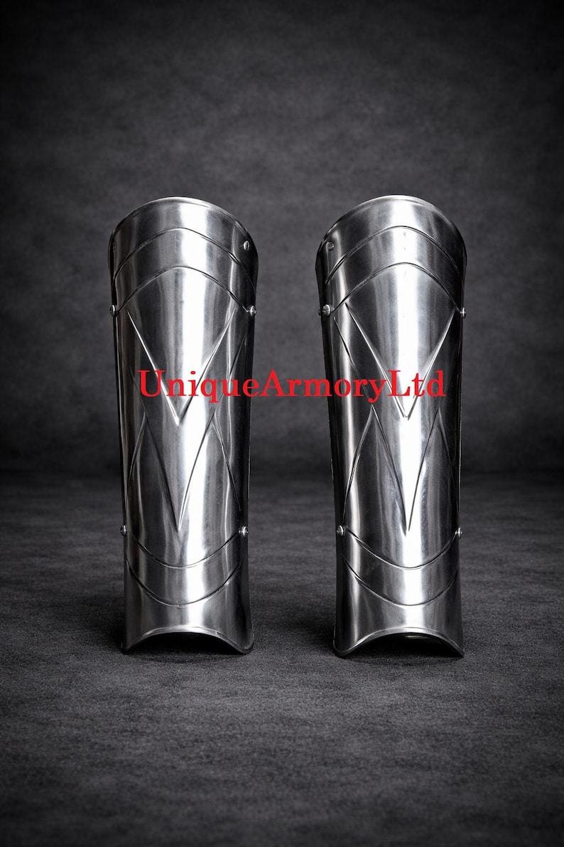 Pu&ograve; includere: Un paio di schinieri in acciaio lucido caratterizzati da un design a cresta verticale a forma di V e rivetti metallici sui lati. Il testo UniqueArmoryLtd &egrave; stampato in rosso al centro di entrambi i pezzi di armatura per la protezione delle gambe.