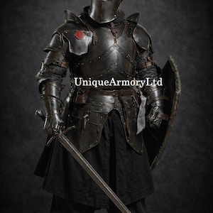 K&ouml;nnte beinhalten: Eine komplette schwarze mittelalterliche R&uuml;stung, einschlie&szlig;lich Helm, Brustplatte und Beinschutz. Der Ritter h&auml;lt ein langes Schwert und einen Schild. Der Text "UniqueArmoryLtd" ist sichtbar.