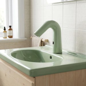 May include: A sage green bathroom sink with a matching curved faucet featuring an integrated motion sensor. The sink is mounted on a light-toned wooden vanity cabinet, and the faucet has a smooth, glossy finish with a small black sensor window.