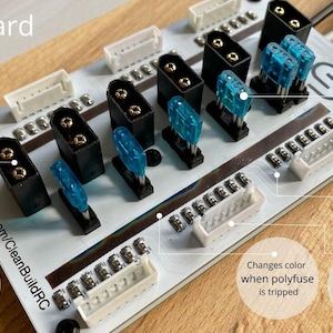 May include: A set of three ceramic mugs with a speckled, cream-colored glaze. Each mug features a different hand-painted floral design in shades of blue, green, and yellow. The mugs have a simple, rounded shape and a comfortable handle.