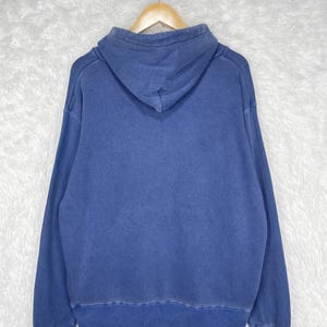May include: A blue hoodie with a drawstring hood, long sleeves, and a ribbed hem and cuffs. The hoodie is hanging on a wooden hanger against a white background.