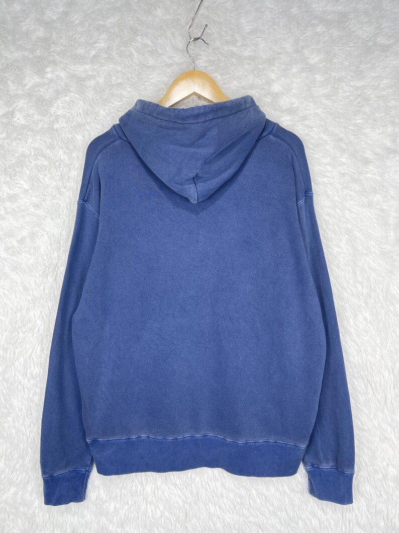 May include: A blue hoodie with a drawstring hood, long sleeves, and a ribbed hem and cuffs. The hoodie is hanging on a wooden hanger against a white background.