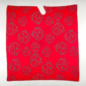 May include: A bright red textile with a repeating pattern of green circular designs. The fabric has a scalloped edge and a cut-out section at the top. The circular designs have intricate details.