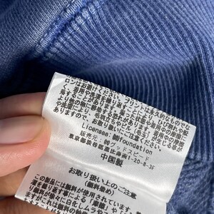 May include: Close-up of a blue fabric with a tag attached. The tag has Japanese text and provides care instructions. The fabric appears to be part of a garment, possibly a sweater or sweatshirt.