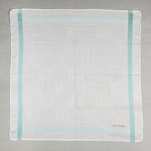 Peut inclure: Mouchoir blanc avec un motif quadrillé subtil et des bordures bleu clair. Le mouchoir est rectangulaire et le texte "pierre balmain" est visible en bas à droite.