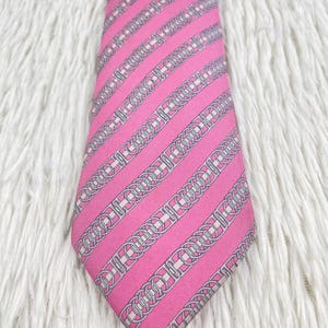 May include: A bright pink necktie featuring a repeating diagonal pattern of silver-toned chain links and interlocking circular motifs. The tie has a pointed tip and a smooth, uniform texture throughout the length of the fabric.