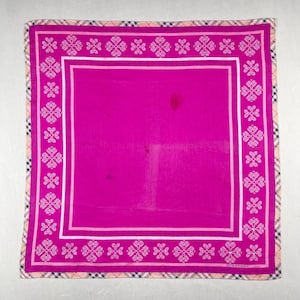 May include: A square, fuchsia-colored scarf with a white floral border and a plaid edge. The scarf has a white inner border and the word "BURBERRY" printed in the bottom right corner.