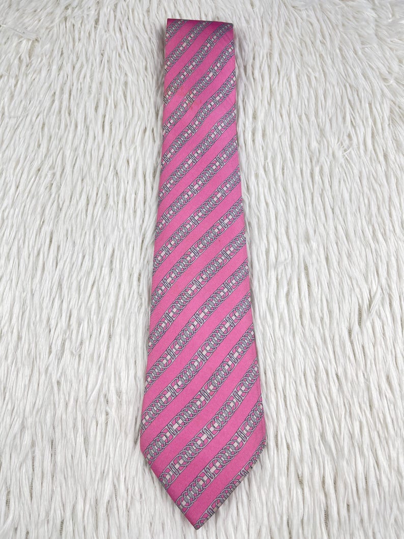 May include: A necktie featuring a vibrant pink base color with a repeating pattern of diagonal silver-grey stripes. Each stripe contains a series of interconnected oval chain-link motifs in white and grey, creating a structured, geometric design.