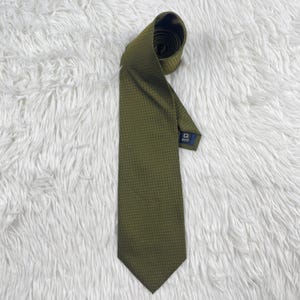 May include: Olive green necktie with a subtle textured pattern. The tie is neatly rolled at the top and lies flat, showcasing its length and design. A small label is visible near the tip. The background is a fluffy white surface.