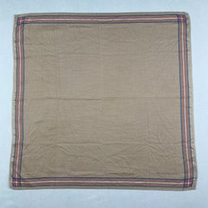 Peut inclure: Foulard carré beige avec une bordure rayée rouge, blanche et bleue. Le foulard porte le texte "PIERRE CARDIN" dans le coin inférieur droit. Le tissu est légèrement froissé.