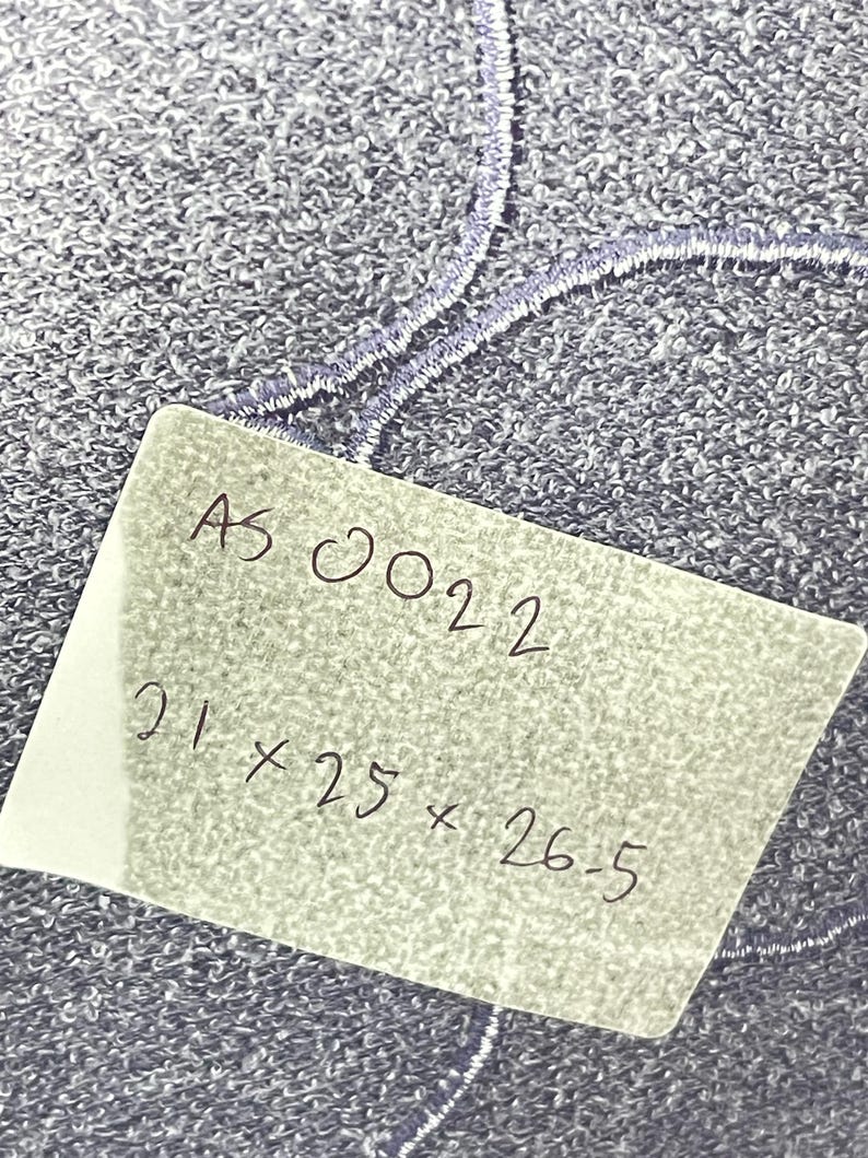 Może przedstawiać: Zbliżenie na teksturowaną, niebieską tkaninę z haftowanymi detalami. Ręcznie napisana etykieta wyświetla tekst "AS 0022" oraz wymiary 21 x 25 x 26,5.