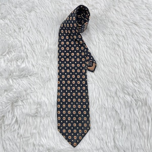 Pode incluir: Uma gravata azul marinho com um padrão repetido de pequenas flores bege com centros vermelhos. A gravata está enrolada no topo e repousa sobre uma superfície branca e fofa. O design da gravata é um estilo clássico e elegante.