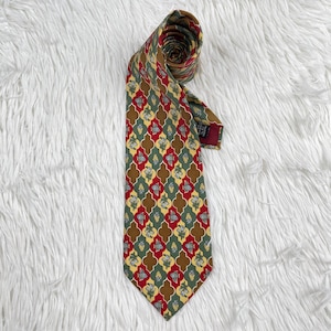 May include: A patterned necktie with a repeating design of red, green, and yellow shapes, including fish and floral designs, on a brown background. The tie is rolled up, showing its intricate pattern.
