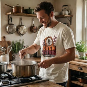 May include: A cream-colored short-sleeve t-shirt featuring a graphic of an orange oven timer with the text OVEN TETRIS Professional Level in bold, distressed lettering. The design includes purple steam rising from the timer.