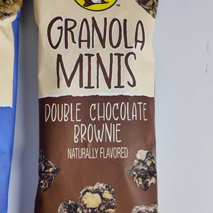 May include: A package of "Granola Minis Double Chocolate Brownie" snacks. The packaging is tan and brown with the brand logo and product information. The net weight is 2 oz (56g).