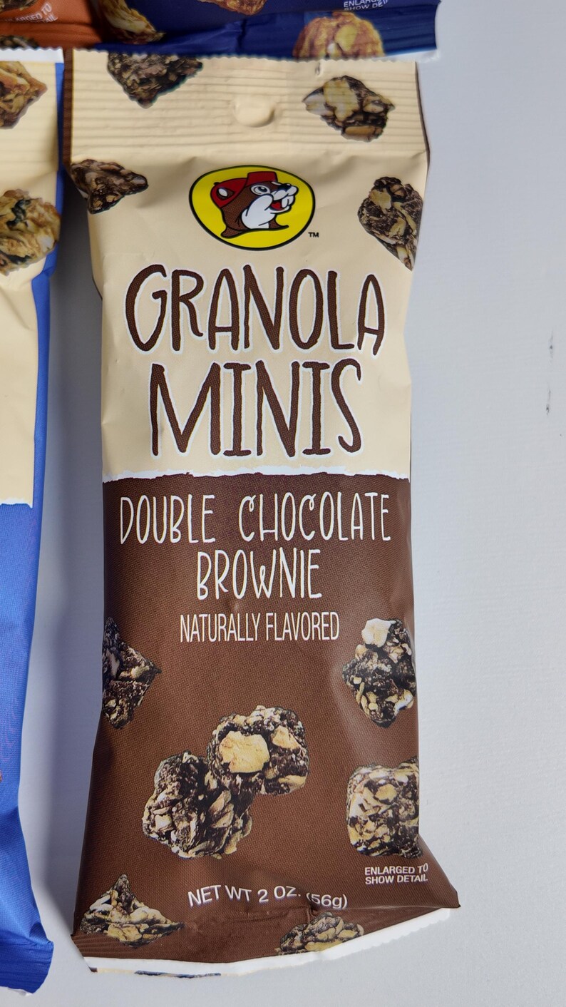 May include: A package of "Granola Minis Double Chocolate Brownie" snacks. The packaging is tan and brown with the brand logo and product information. The net weight is 2 oz (56g).