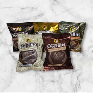 May include: Assortment of Buc-ee's OverBite chocolate candies in various flavors. Packages include Dark Chocolate, Dark Chocolate Peanut Butter, and Dark Chocolate Cookies & Cream. Each package features the Buc-ee's logo and product information.