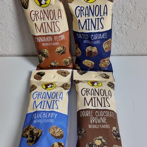 May include: Four bags of Granola Minis in Cinnamon Pecan, Salted Caramel, Blueberry, and Double Chocolate Brownie flavors. Each bag features a cartoon beaver logo and the words "Granola Minis". The bags are 2 oz (56g) each.