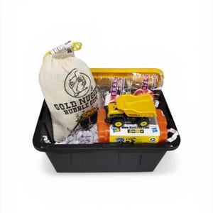 May include: A black plastic basket filled with a toy dump truck, bubble gum, and candy. The toy truck is yellow and black. The bubble gum is in a beige bag with the words "Gold Nugget Bubble Gum".
